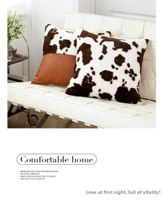 Detail of cow print plush pillow cover with brown faux leather patch on leather sofa