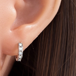 Silver huggie earrings with five round white opal stones on model ear view