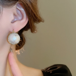 Gros plan sur boucle d'oreille en perle baroque avec cadre doré sur l'oreille