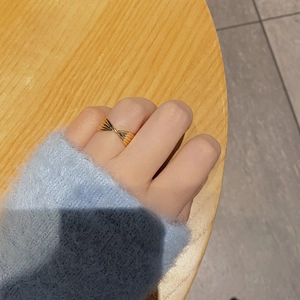 Macro detail of a twisted gold ring worn on a finger against a blue sweater and wooden desk