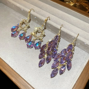 Detailed macro view of gold-tone leaf and purple crystal droplet fringe earrings in a tray