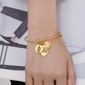 Detail of adjustable gold metal bracelet with heart, girl, and lotus charms