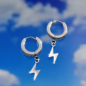 Detail view of silver stainless steel lightning bolt pendant earrings against blue sky