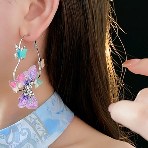 Gros plan de créoles argentées ornées de charms papillons colorés et scintillants sur mannequin