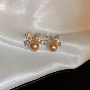Détail macro de boucles d'oreilles nœud doré avec strass brillants et perle champagne