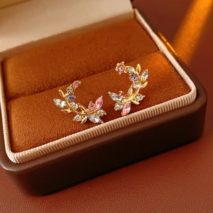 Detailed close-up of golden leaf earrings with multicolored crystals in a velvet box