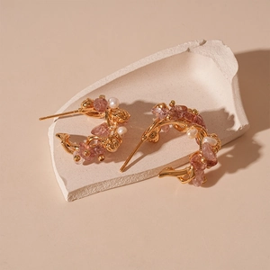 Detailed close-up of C-shaped earrings with strawberry quartz and pearls on golden base