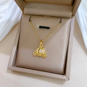 Detailed close-up of golden pumpkin carriage necklace with sparkling crystal in a jewelry box