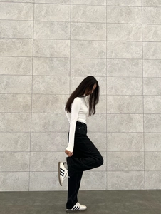 Detail einer schwarzen High-Waist-Hose mit weitem Bein und weißem Langarm-Oberteil
