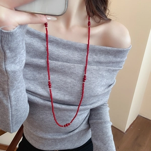 Close-up of long layered red crystal beaded necklace worn over a grey knit sweater