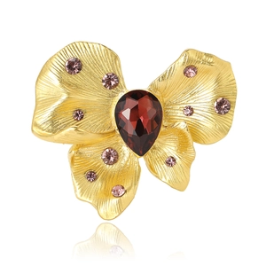 Golden butterfly brooch with red teardrop gemstone and purple crystals on white background