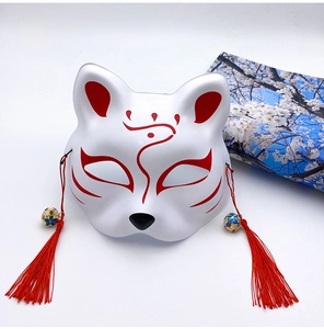 Detailed close-up of a Japanese Kitsune mask with red hand-painted patterns and tassels