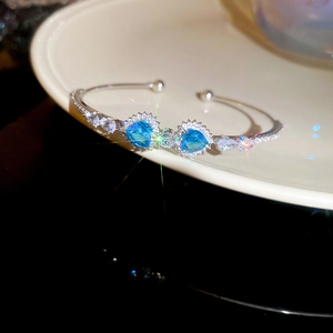 Detail of silver heart bangle with blue zircon stone resting on a ceramic dish