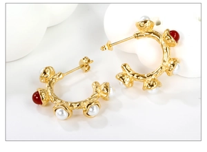 Detail of gold hoops with irregular texture, white pearls and a red gemstone inlay
