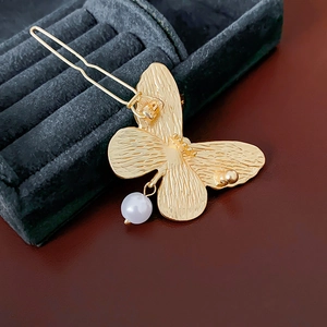 Detail of golden butterfly hair clip with pearl charm on dark green velvet box