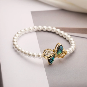 Detailaufnahme von Perlenarmband mit goldenem Schmetterling und irisierender Muschel