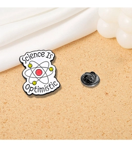 Detail of metal science pin with Science Is Optimistic text and atom design
