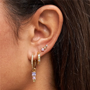 Close-up of gold stacking earrings with purple and white crystals on model ear