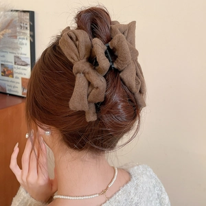 Rear view of model wearing a brown fabric bow hair claw clip in a minimalist home setting