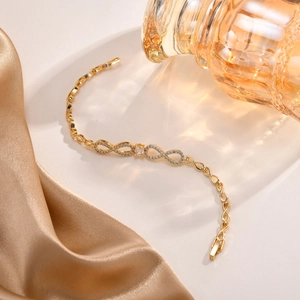 Detail eines goldenen Unendlichkeitsarmbands mit Zirkonia auf Satin und Glashintergrund