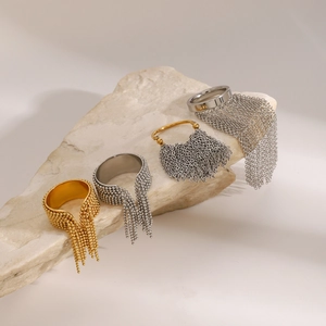 Detail view of gold and silver stainless steel tassel rings on a textured stone surface