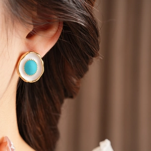 Close-up of vintage gold stud earrings with white enamel and sky blue center stone