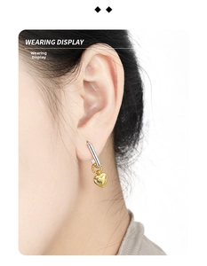 Detailed view of bicolor S925 silver earring with golden heart pendant on model