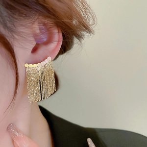 Close-up of elegant gold fan-shaped stud earrings with long metal chain tassels worn on ear