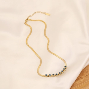 Golden snake chain necklace with blue evil eye beads on soft beige silk background