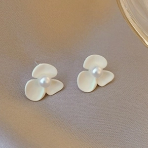 Detail of matte white flower earrings with center pearl on a textured fabric background