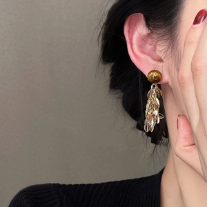 Detailed view of gold tassel earrings with resin beads and metallic leaf pendants