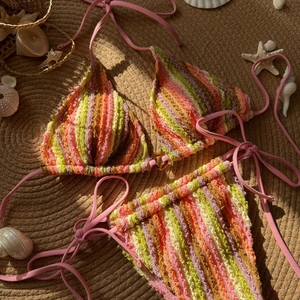 Détail de bikini au crochet à rayures avec accessoires de plage sur un tapis de paille