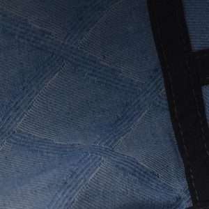 Macro detail of blue denim fabric texture and black stitched inner seam of the beret