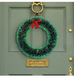 Detail of a Christmas wreath with green tinsel and a red bow on a dark green door