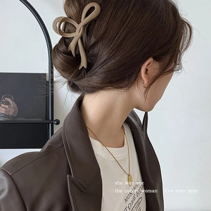 Large matte khaki bow hair claw clip for elegant bun hairstyles on model in indoor setting
