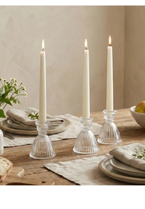 Close-up of vintage ribbed glass skirt candle holder with a white taper candle on a wooden table