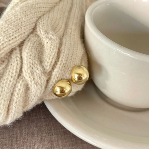 Polished gold sphere stud earrings pinned on a beige knitted sweater and white cup