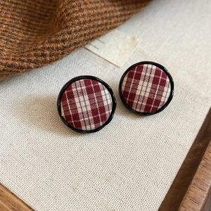 Close-up of red plaid fabric round stud earrings with elegant black metal frames