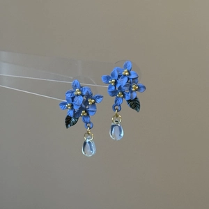 Macro view of blue flower stud earrings with golden stamens and clear teardrop bead details