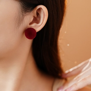 Detail of red flocked circular earring showing soft velvet texture on a model's ear