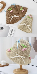 Detail of hand-woven straw hats with crochet cherry accents and blue ribbon decoration