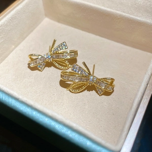 Macro shot of gold bow stud earrings with sparkling zircons on soft velvet padding