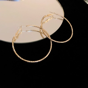Macro detail of gold hammered hoop earrings with textured finish on black velvet surface