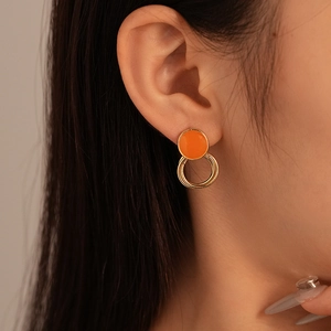 Close-up of model wearing orange and gold geometric stud earrings with polished metal finish