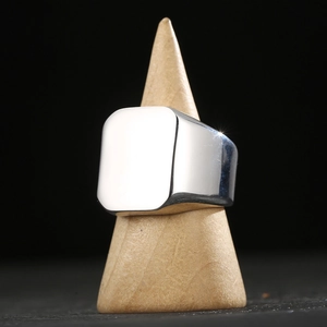 Polished titanium steel signet ring with rectangular face on wooden stand