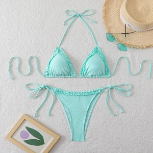 Close-up of mint green striped bikini set with ruffled edges on white plush rug