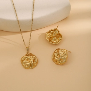 Detailed view of gold geometric heart necklace and stud earrings with leaf texture