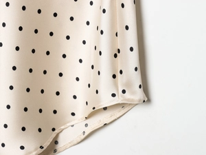 Détail du tissu satiné crème à pois noirs avec des finitions de couture de précision