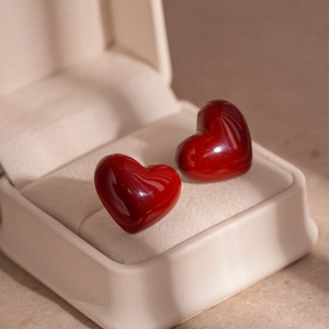Close-up of glossy red 3D heart stud earrings placed in a beige leather jewelry box