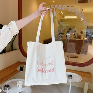 Gros plan d'un sac cabas en toile blanche avec broderie 'beloved' rose dans un café cosy